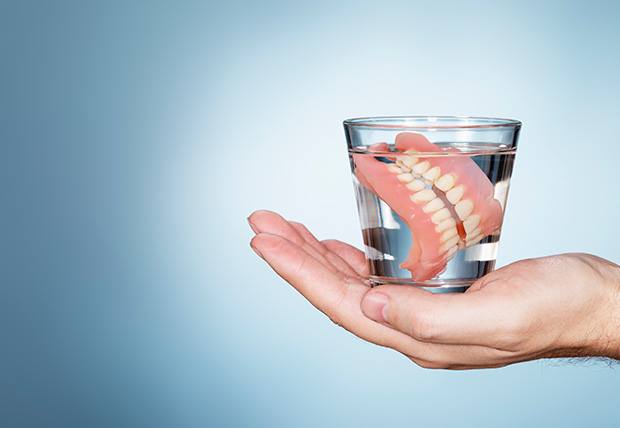 Someone holding dentures in a jar