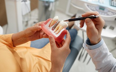 A patient holding tooth model while a dentist explains dental implant recovery