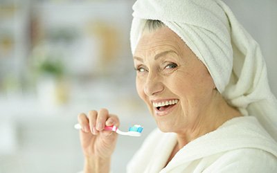 An older woman in a bathrobe brushing her teeth